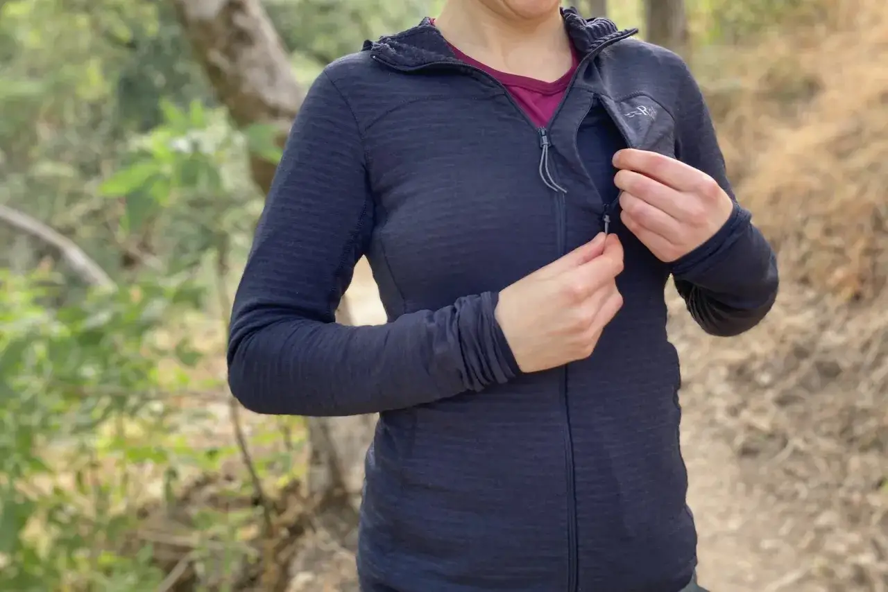 Frau schließt Reißverschluss einer dunkelblauen Fleecejacke. Das Material ist weich und warm, ideal für Outdoor-Aktivitäten.