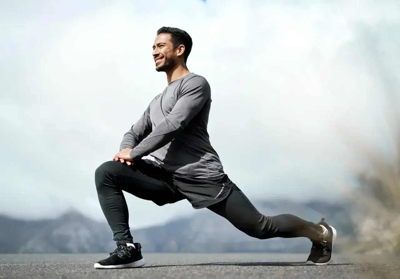 Un homme souriant effectue une s&eacute;ance stretching en plein air, profitant d'un paysage montagneux.
