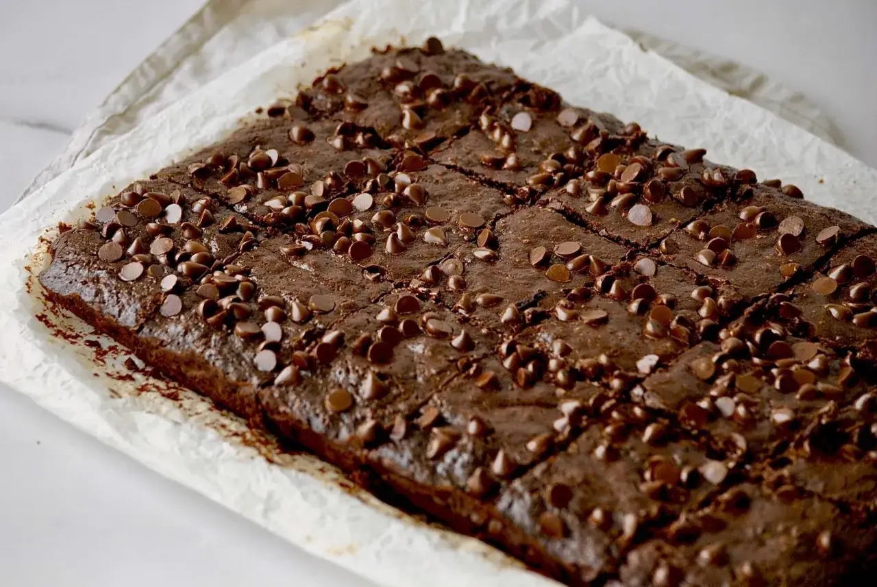 Saftige Zucchini-Brownies, bestreut mit vielen Schokost&uuml;ckchen, auf Backpapier.
