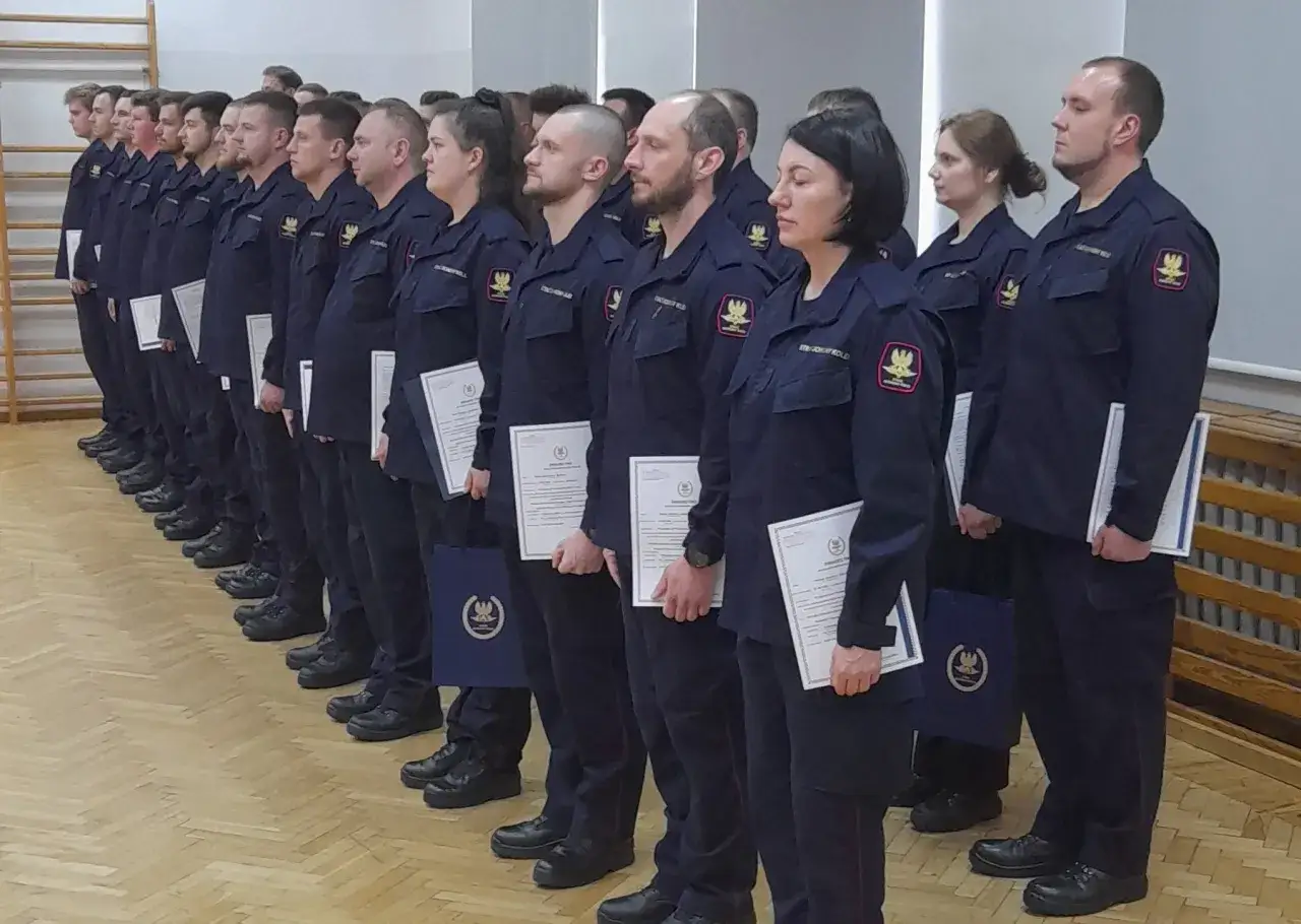 Grupa funkcjonariuszy Straży Ochrony Kolei w mundurach, stojąca w szeregu, odbiera dyplomy.
