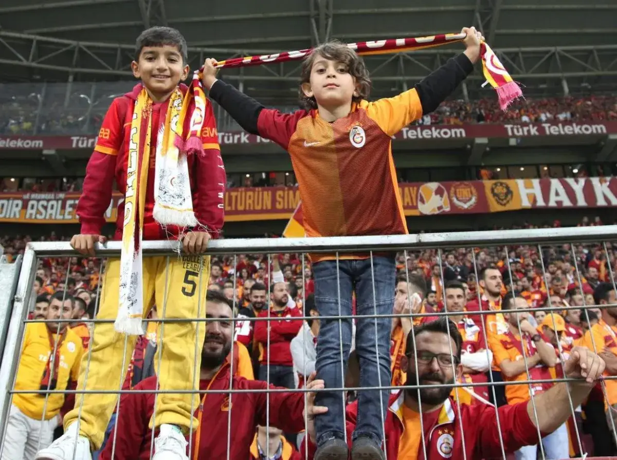 Dwóch chłopców w barwach tureckich klubów piłkarskich, Galatasaray, kibicuje na trybunach.