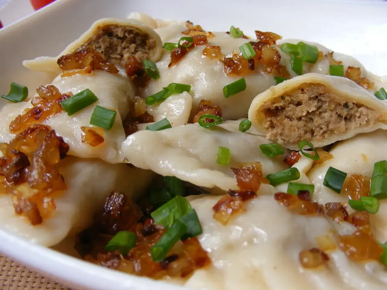 Pyszne pierogi z mięsem, posypane skwarkami i szczypiorkiem, kuszą swoim domowym wyglądem.