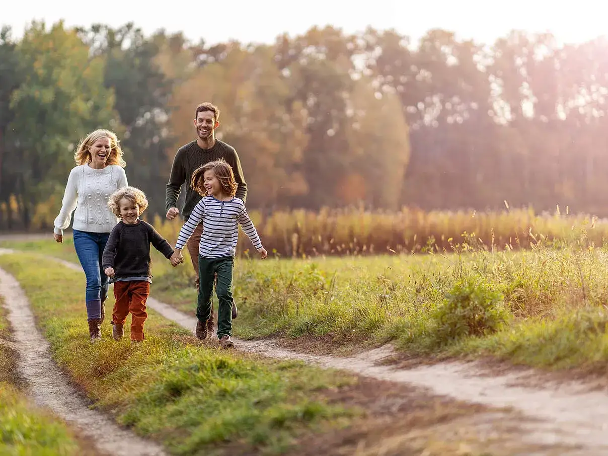 Gl&uuml;ckliche Familie mit zwei Kindern, die auf einem Feldweg spazieren gehen. Tolle Unternehmungen mit Kleinkind 2 Jahre im Herbst.