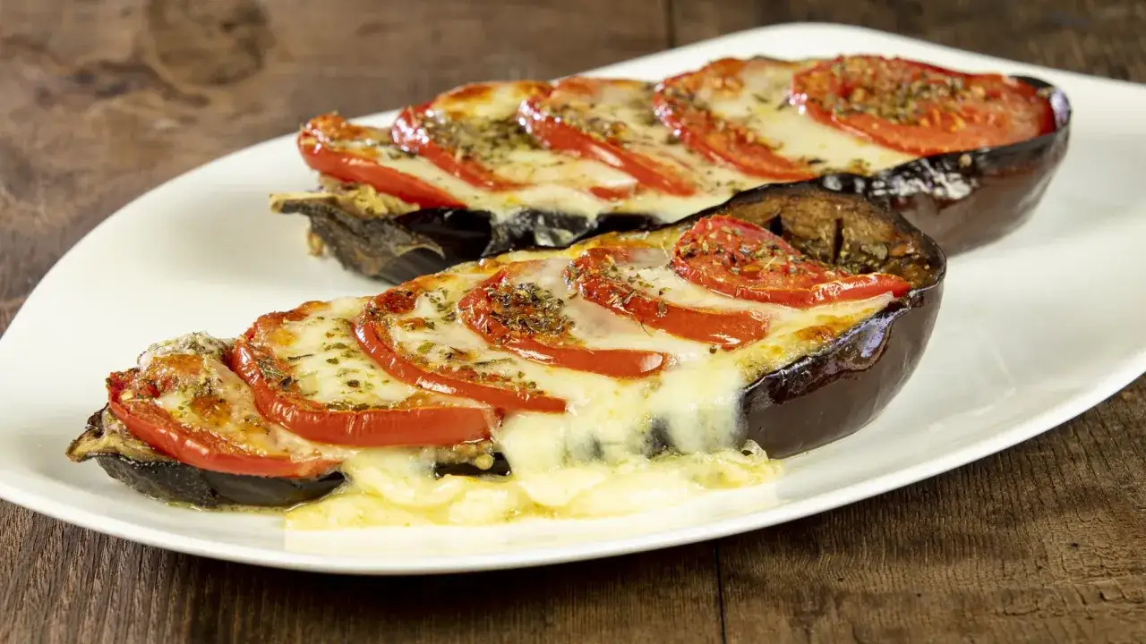 Melanzane ripiene senza carne, con pomodoro e formaggio filante, su un piatto bianco.