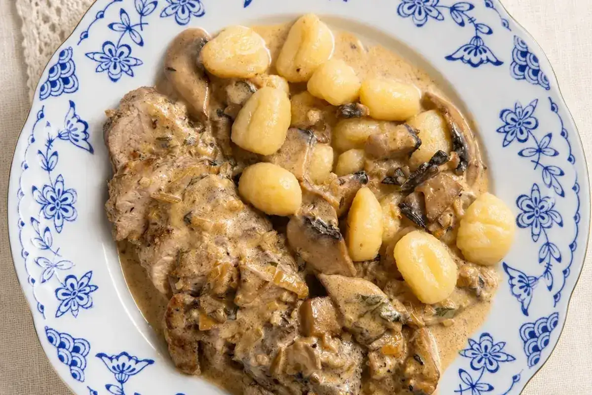 Miękkie polędwiczki wieprzowe w sosie grzybowym z kluskami gnocchi na talerzu z niebieskimi wzorami.