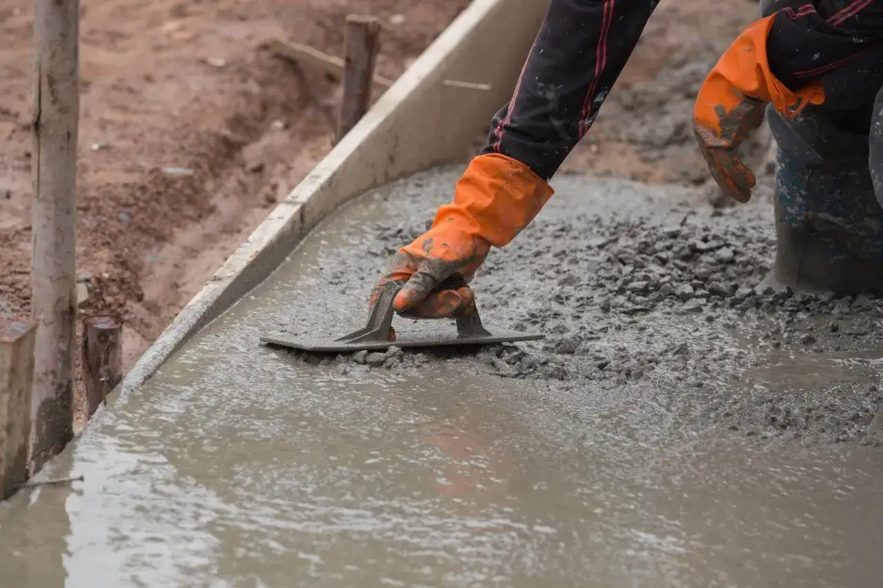 Ręka w pomarańczowej rękawicy wygładza świeży beton kielnią. To kluczowy etap budowy, gdzie dysperbent zapewnia trwałość nawierzchni.