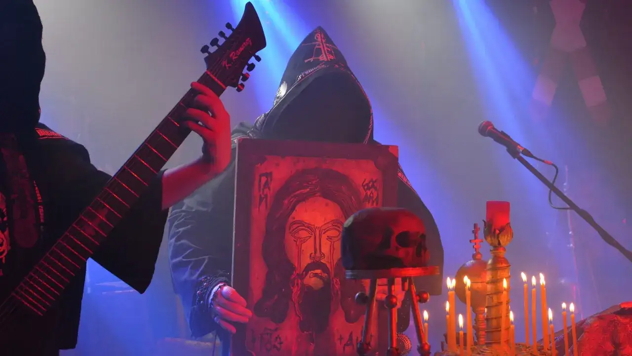 Batiuszka zespół na scenie z ikoną Jezusa, czaszką i świecami. Muzyk gra na gitarze.