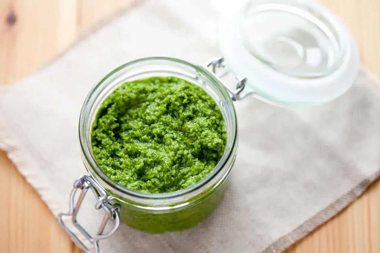 Słoik pełen intensywnie zielonego, domowego pesto z jarmużu, gotowego do podania.