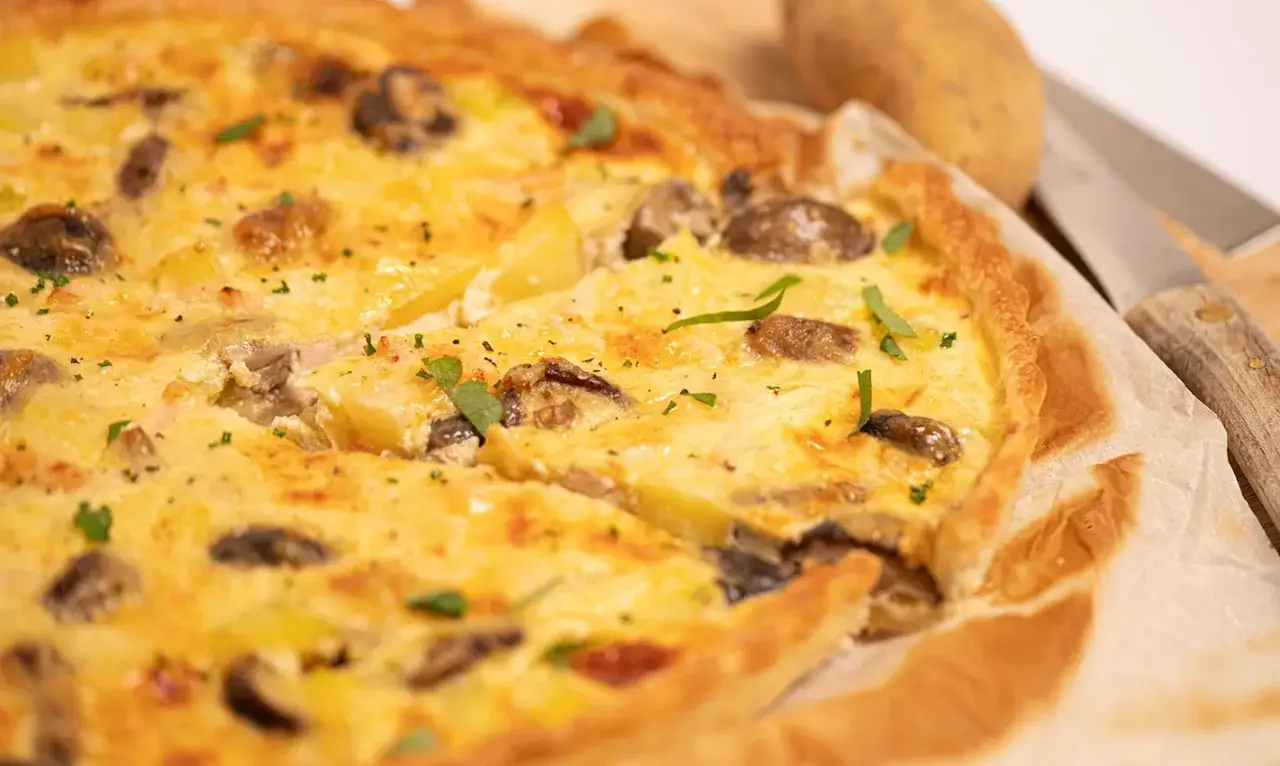 Une délicieuse quiche poulet pomme de terre, garnie de champignons et d'herbes fraîches, prête à être dégustée.