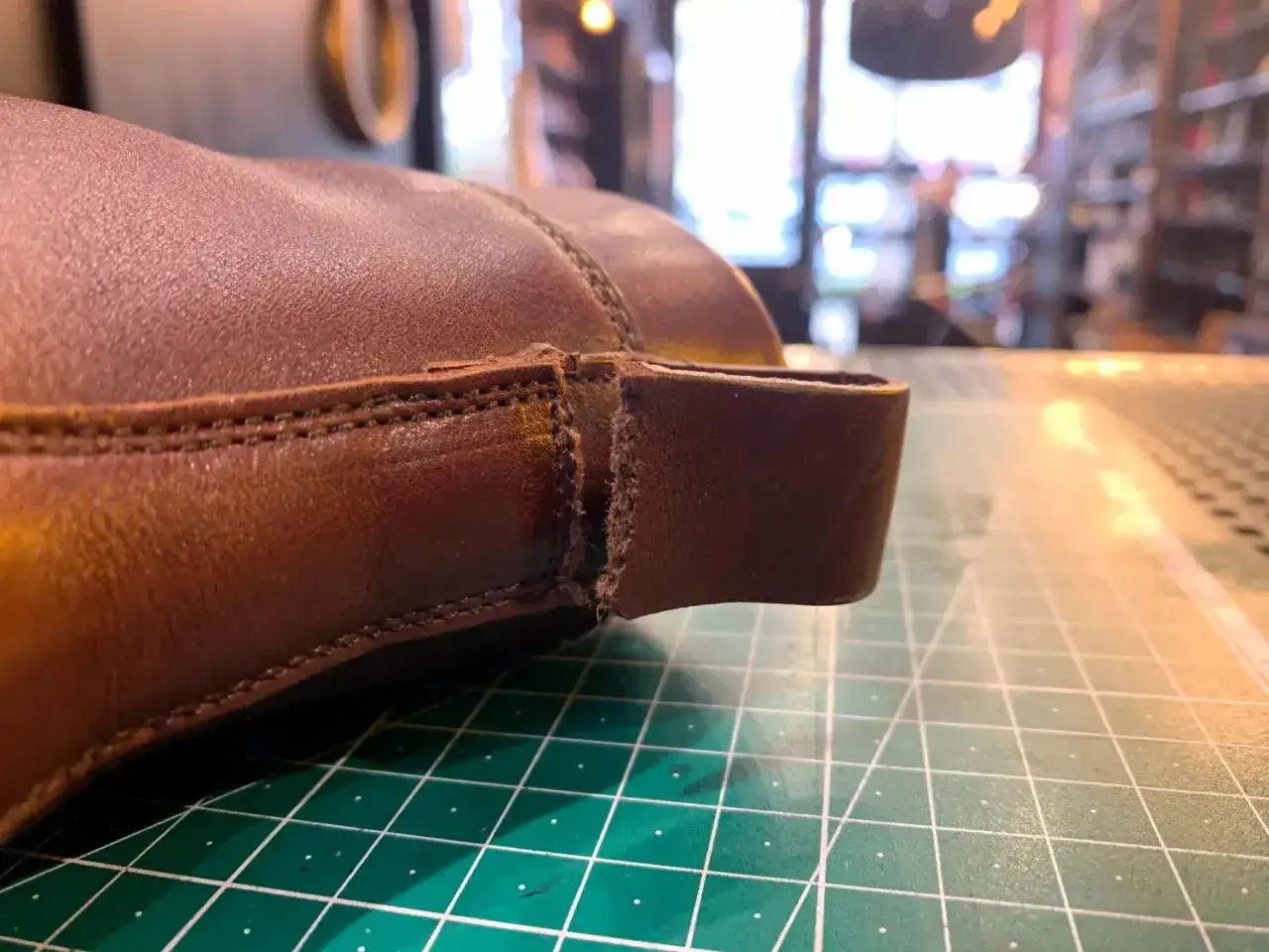 Gros plan sur une chaussure en cuir marron dont le cuir s'effrite au niveau de la languette arrière, sur un tapis de découpe vert.