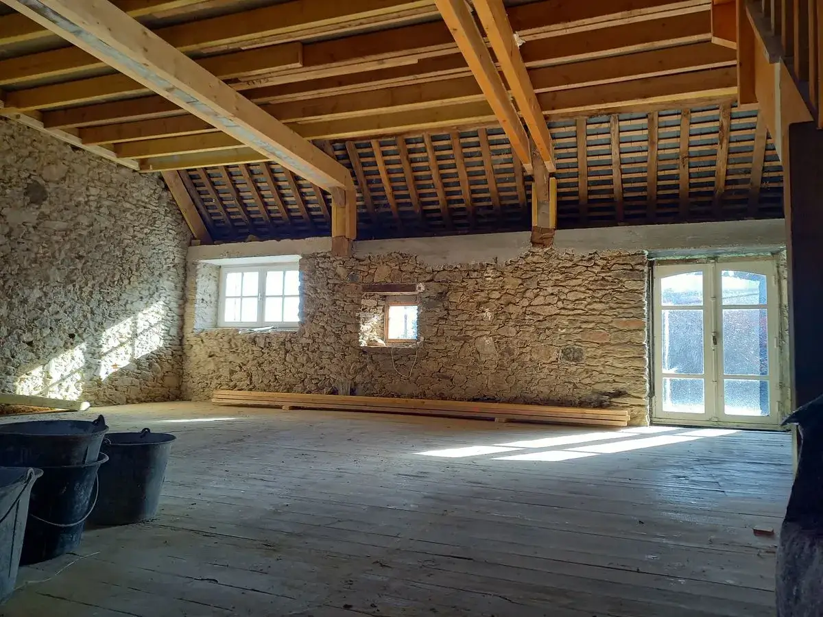 Intérieur d'une maison en rénovation, murs en pierre, poutres apparentes. Un projet pour savoir comment assainir une maison.
