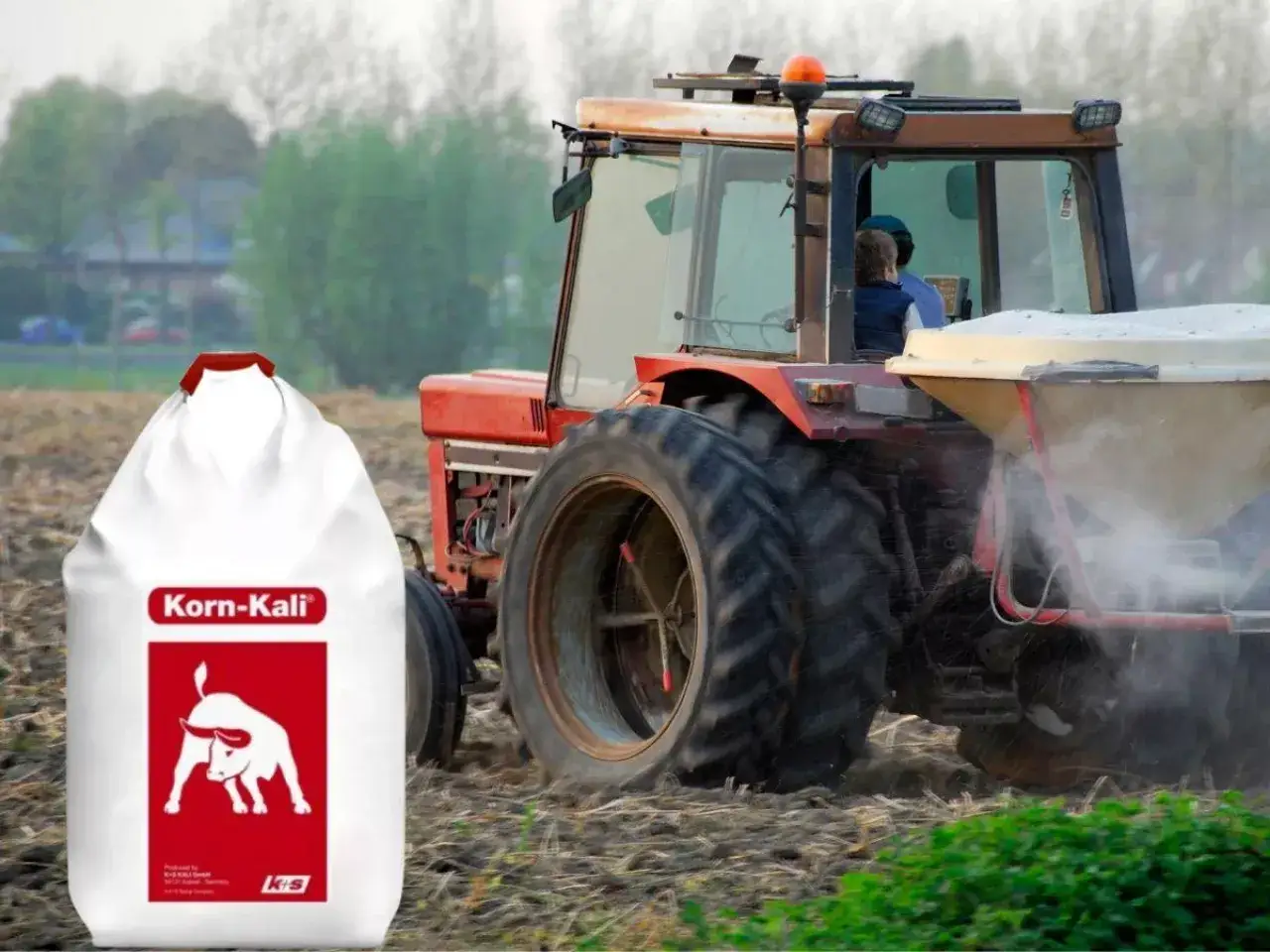 Worek z nawozem Korn-Kali obok traktora rozsypującego nawóz na polu.