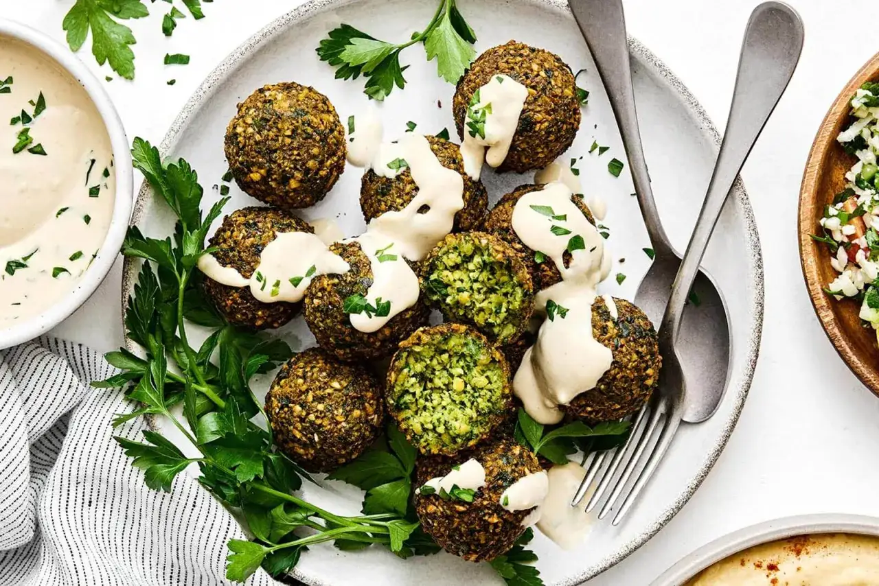 Falafel co to? Aromatyczne kulki z ciecierzycy, polane kremowym sosem tahini, ozdobione świeżą pietruszką. Pyszna przekąska!