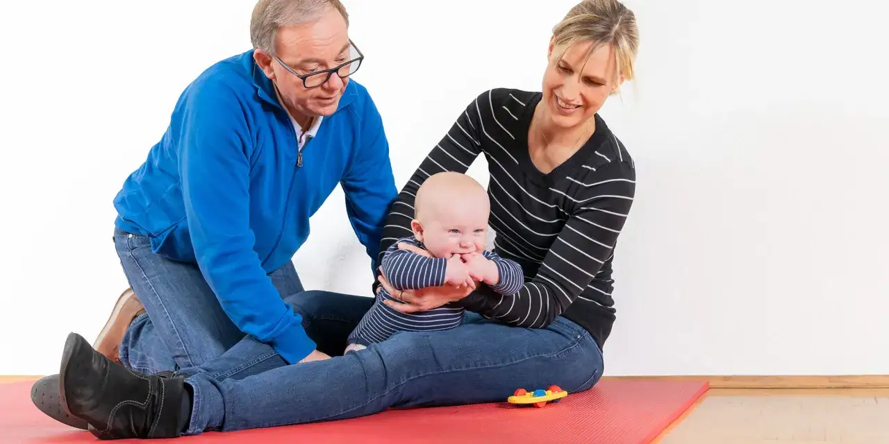 Ein Mann und eine Frau üben mit einem Baby auf einer roten Matte. Die kg zns kinder sind glücklich.