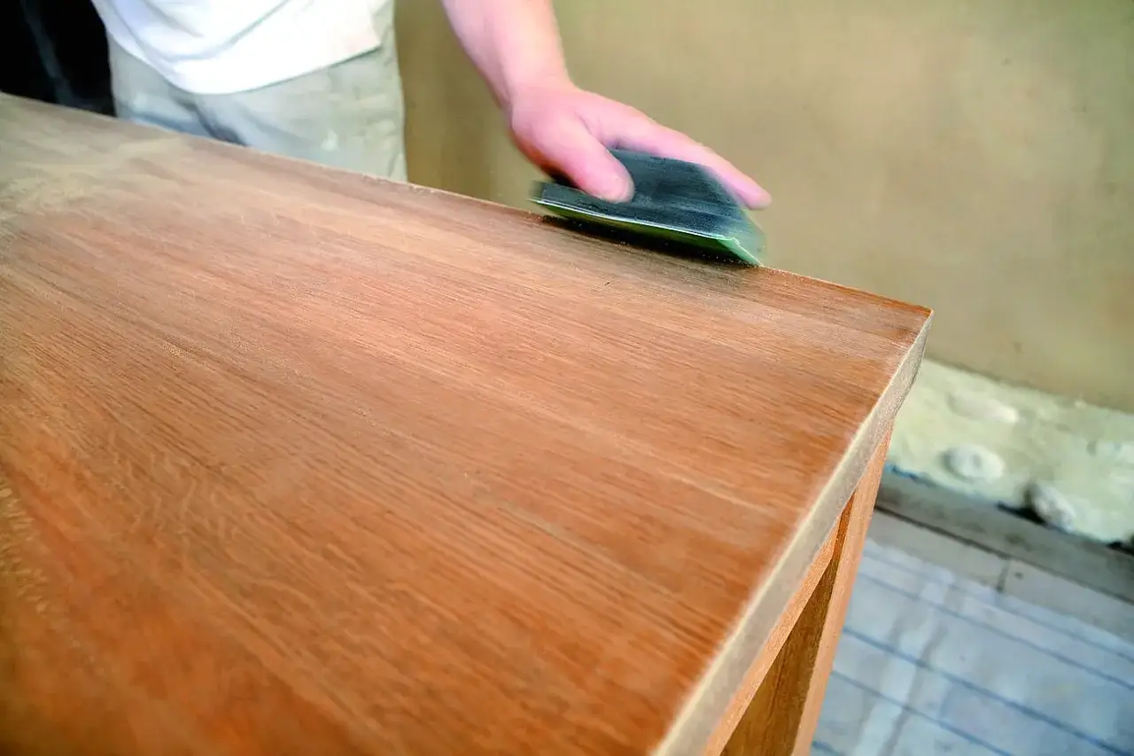 Main d'artisan pon&ccedil;ant un meuble en bois, pr&eacute;parant la surface pour une peinture &agrave; l'huile sur bois technique.