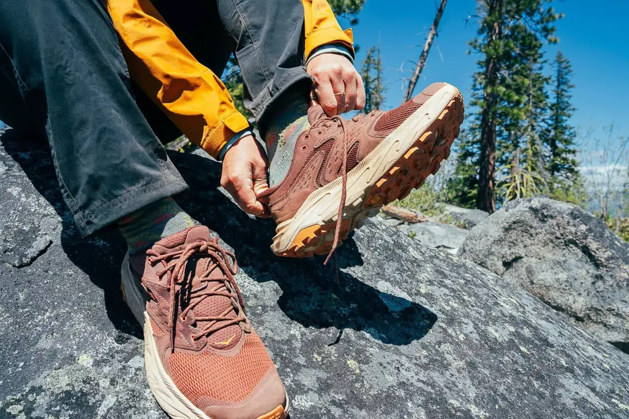 Lacing up sturdy hiking boots on a rocky trail. These boots are essential for grip and support on uneven terrain, ensuring a safe and comfortable adventure.