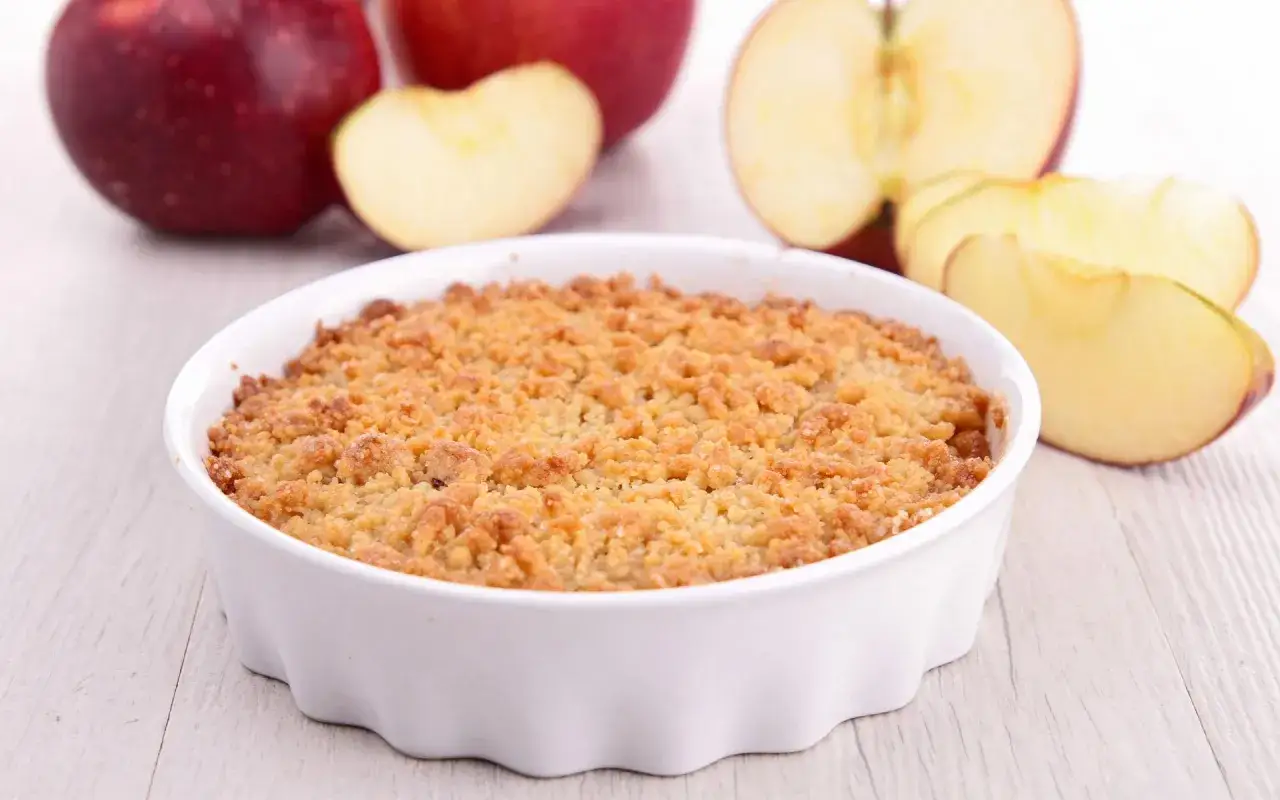 Un délicieux crumble pomme individuel doré et croustillant, prêt à être dégusté. Des pommes fraîches en arrière-plan.