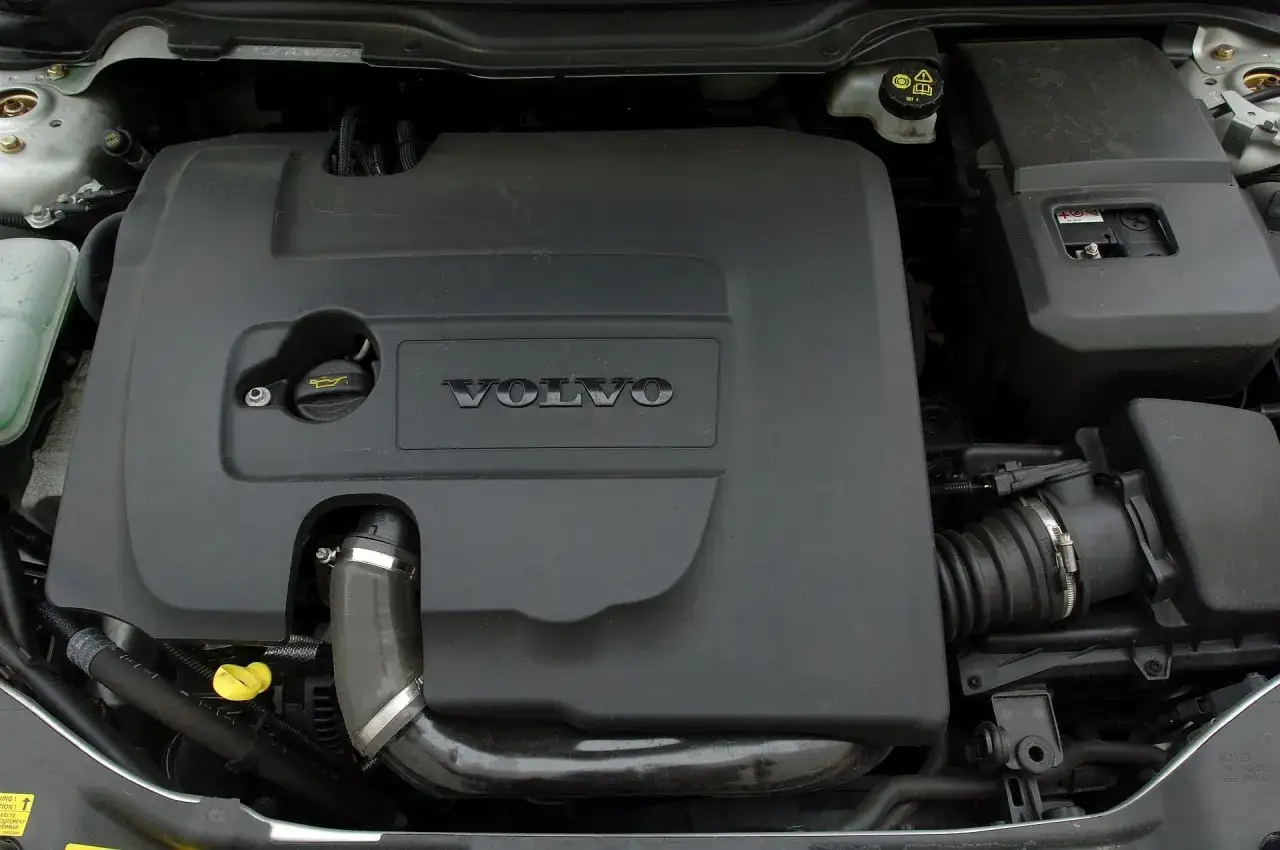 Silnik Volvo V50 z widocznym logo marki. Czarna osłona silnika, korek oleju i elementy układu dolotowego.
