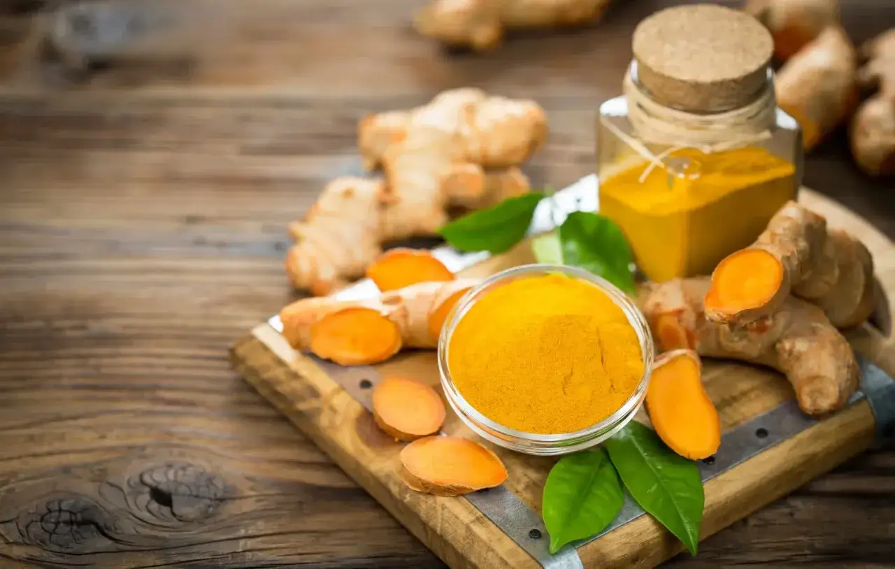 Racines de curcuma frais et poudre dor&eacute;e dans un bol, pr&ecirc;ts &agrave; &ecirc;tre m&eacute;lang&eacute;s avec du miel pour une potion bien-&ecirc;tre.