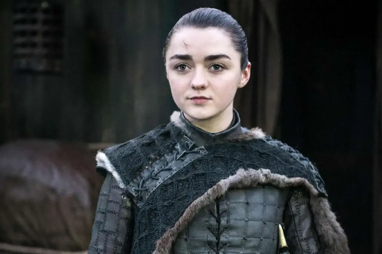 Maisie Williams som Arya Stark, med ett ärr i pannan, bär en mörk, pälsfodrad rustning.