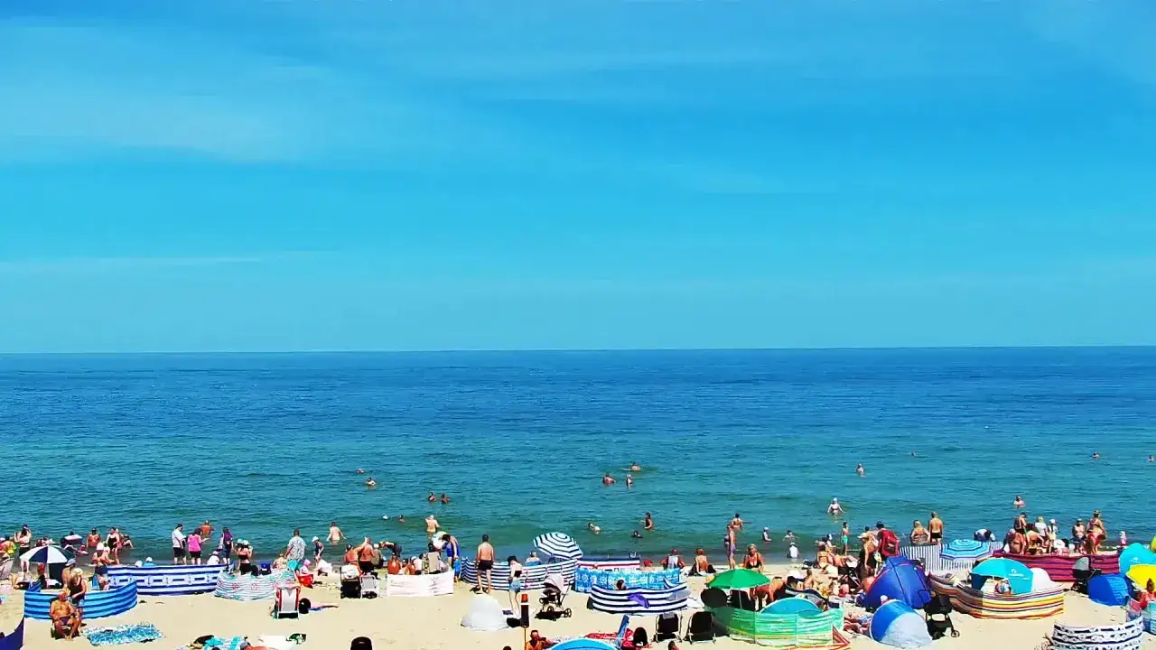 Władysławowo co zobaczyć? Tłoczna plaża, ludzie kąpią się w morzu i opalają pod kolorowymi parawanami.