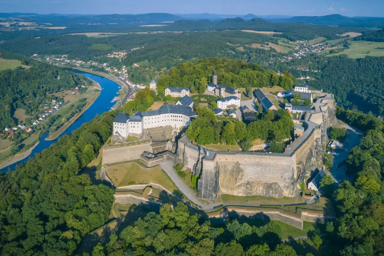 Imponująca twierdza Königstein na skalistym wzgórzu, otoczona zielenią i rzeką Łabą.