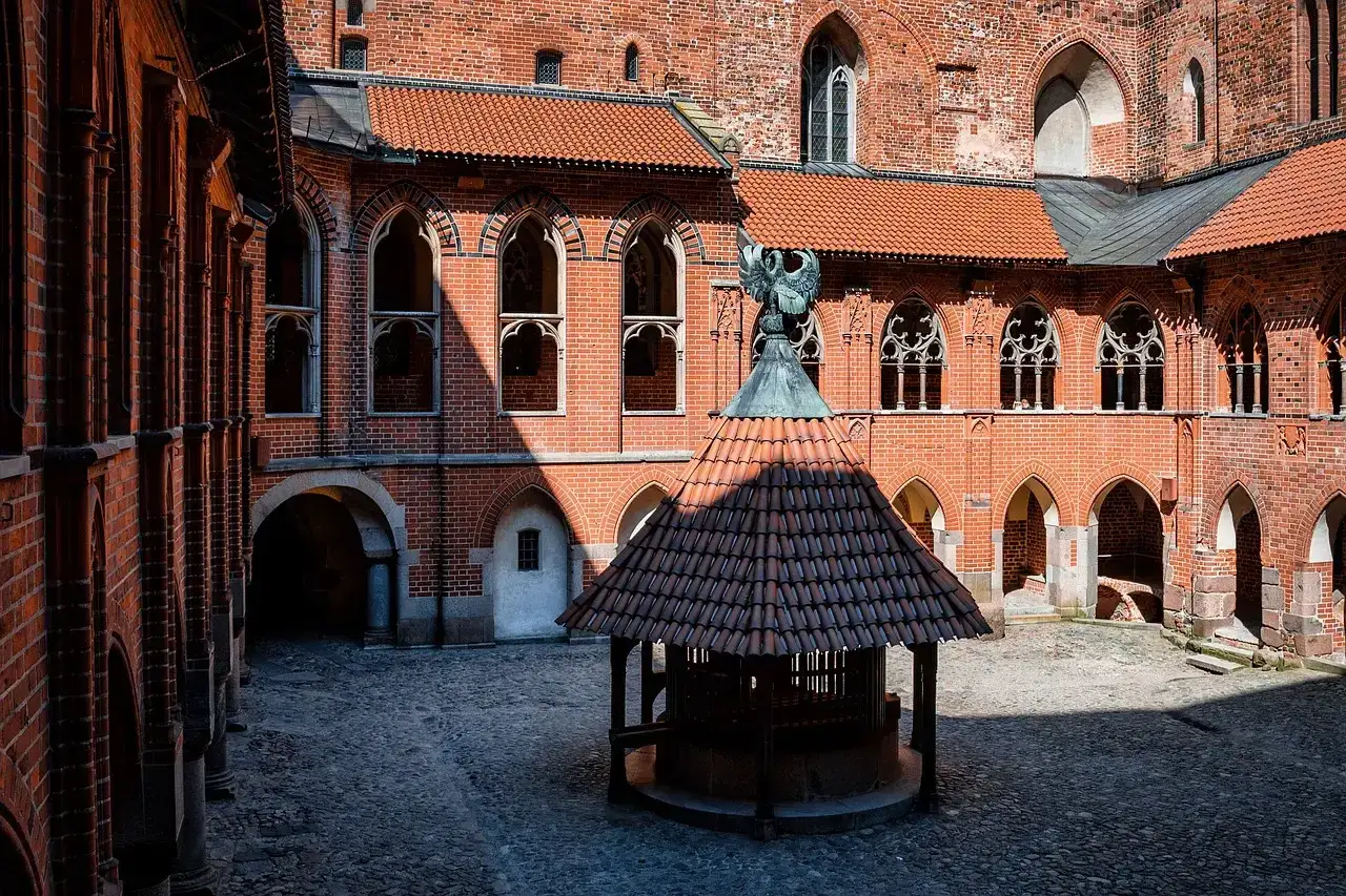 Dziedziniec zamku w Malborku, z kamienną studnią i ceglanymi arkadami. Zamek w Malborku zdjęcia.