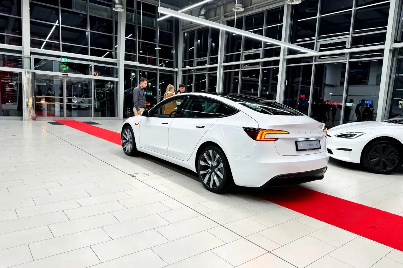 Białe Tesla modele Model 3 i Model S na czerwonym dywanie w salonie.