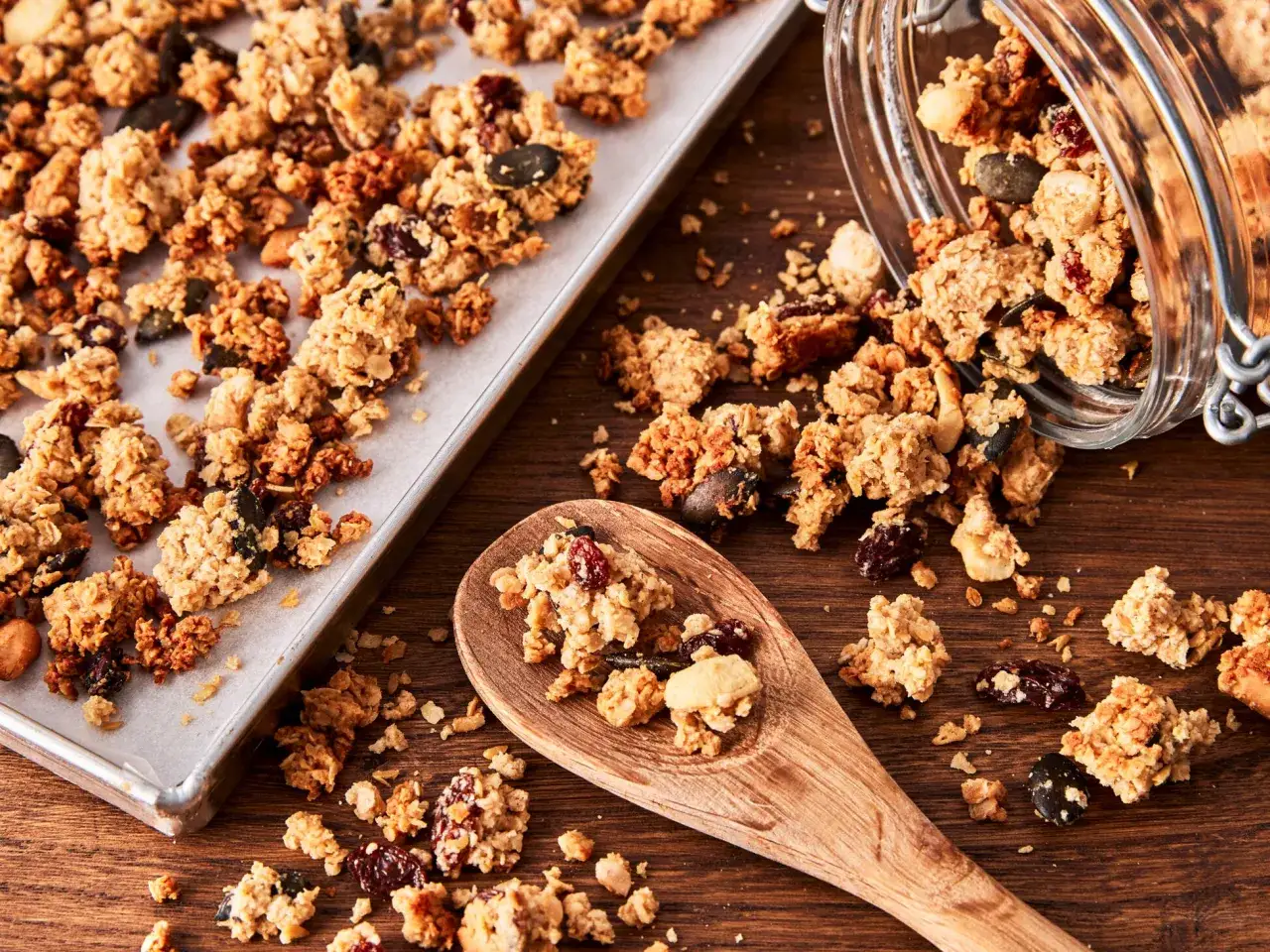 Knuspriges, selbstgemachtes Granola mit Nüssen und Trockenfrüchten auf einem Backblech und einem Holzlöffel. Perfekt zum Frühstück!
