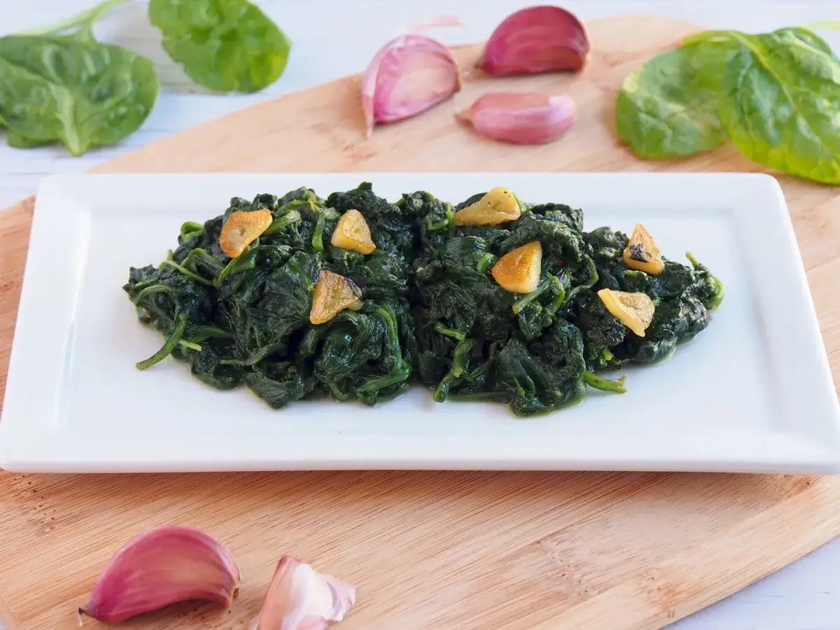 Deliciosas espinacas salteadas con ajo, servidas en un plato blanco sobre una tabla de madera.