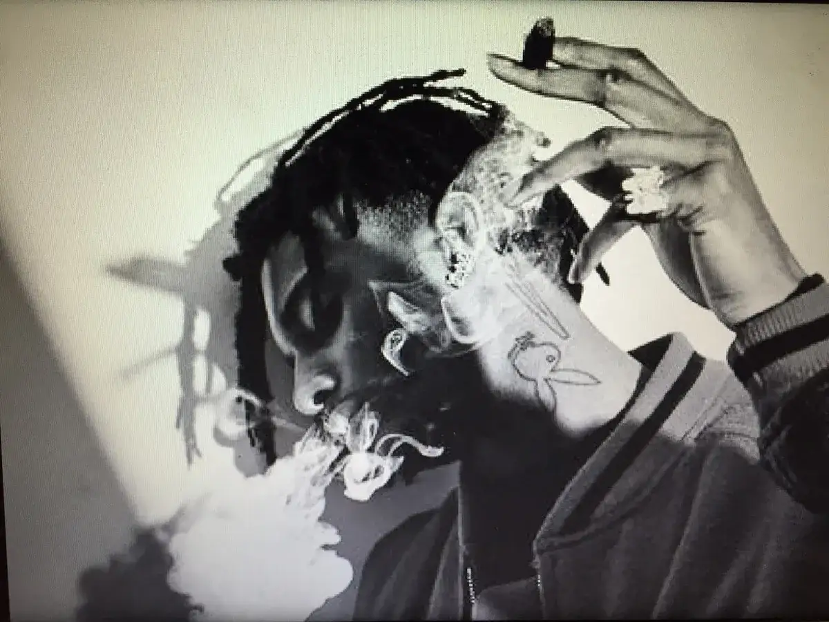 Playboi Carti wiek. Młody raper z dredami, palący cygaro, z tatuażem Playboya na szyi.