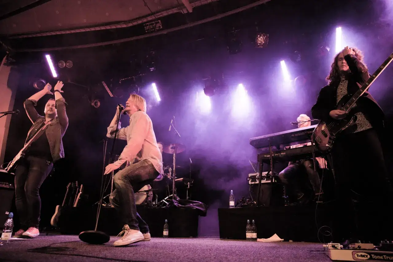 Tommy Nilsson band spelar live med intensiv belysning. En gitarrist och s&aring;ngare i f&ouml;rgrunden, en basist och keyboardist i bakgrunden.