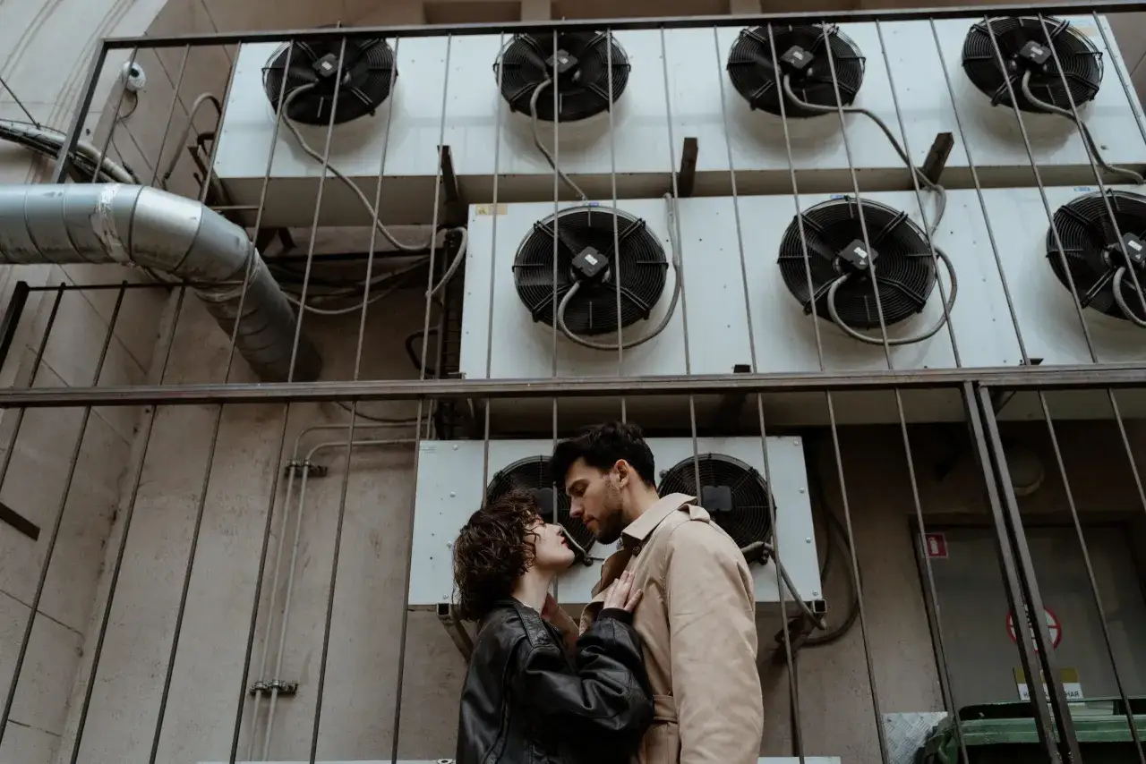 Un couple s'embrasse devant des unités de climatisation. Mon ex m'aime encore, mais il a une copine.
