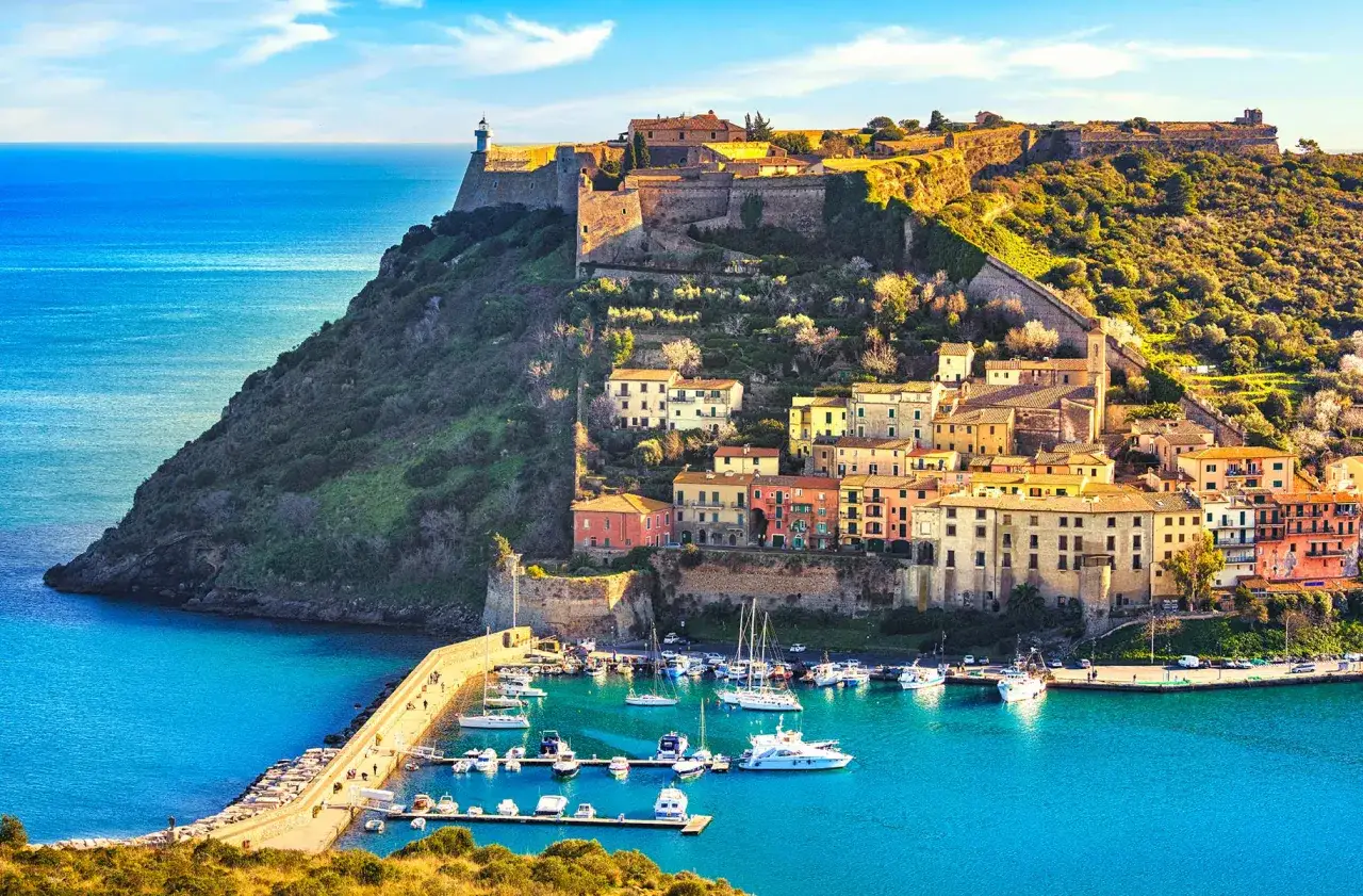 Un borgo colorato su una collina con un faro domina un porto pieno di barche. Un paesaggio incantevole, come quelli che si possono trovare a Rimini e dintorni.
