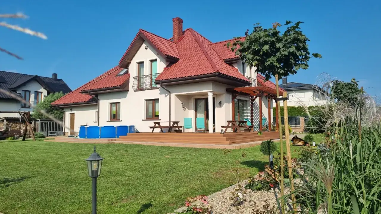 Nowoczesny dom z czerwonym dachem, tarasem, basenem i ogrodem.