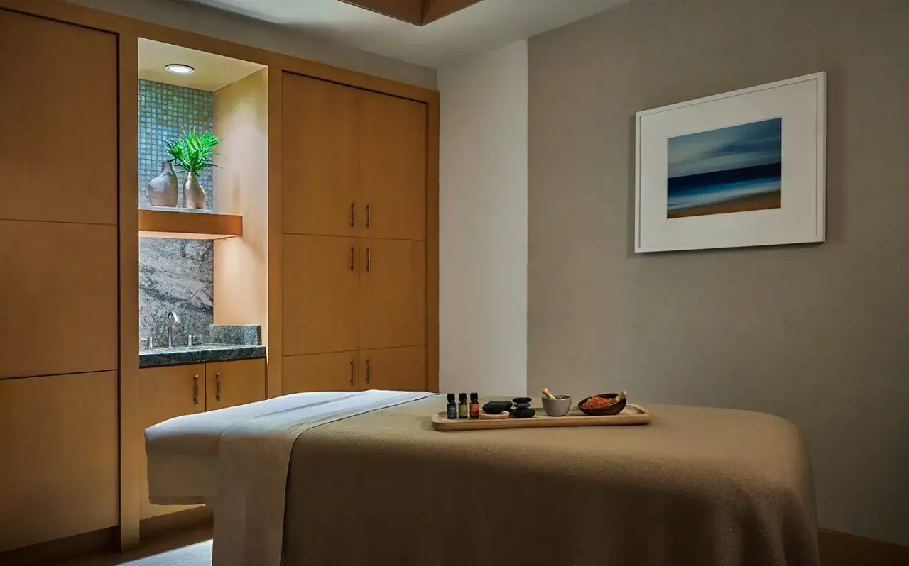 A spa room with a massage table set for a facial or massage first. Essential oils, stones, and a bowl of salts are on a tray.