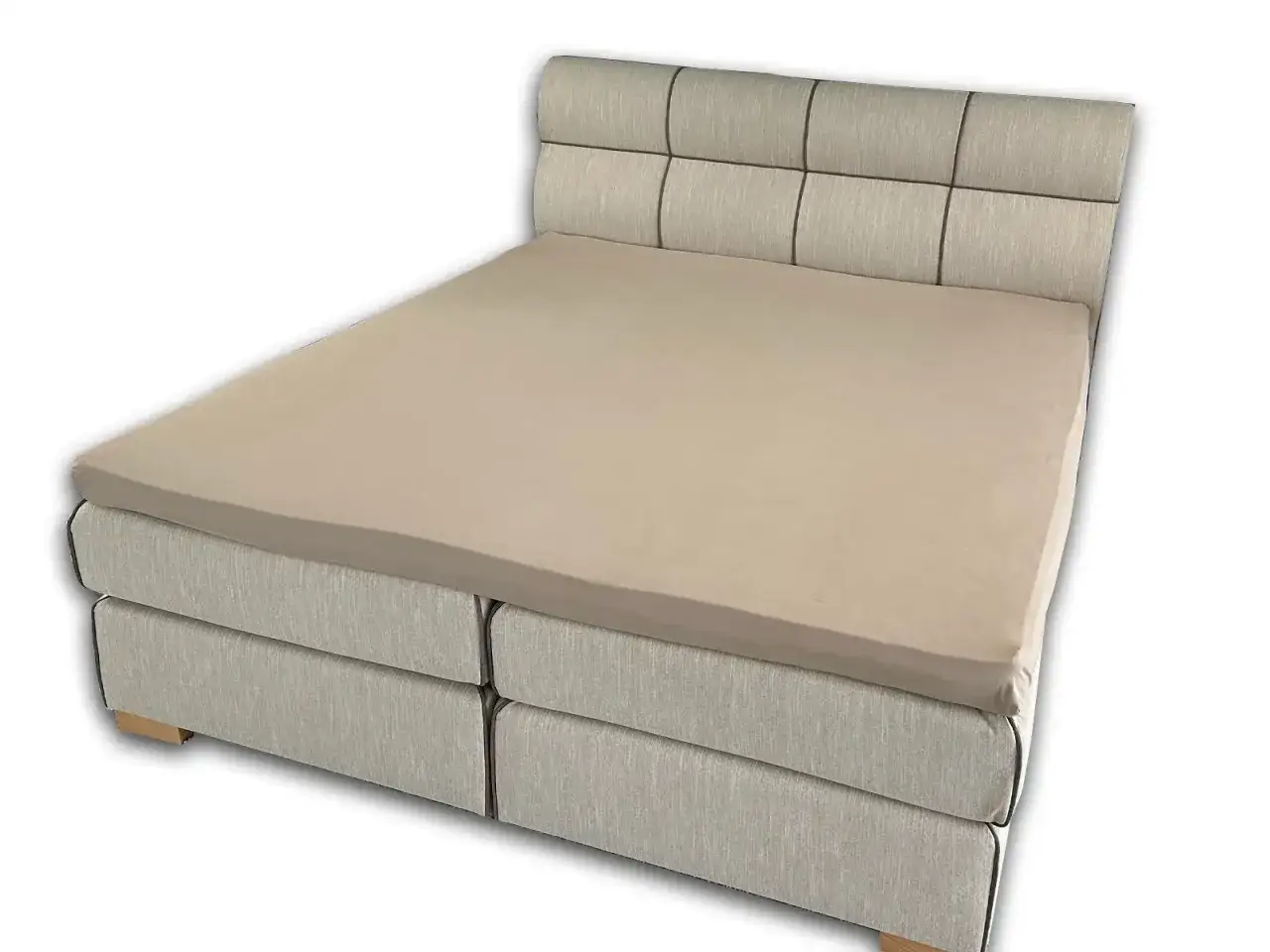 Ein hellbraunes Spannbettlaken wird &uuml;ber eine Matratze eines Boxspringbetts gezogen.