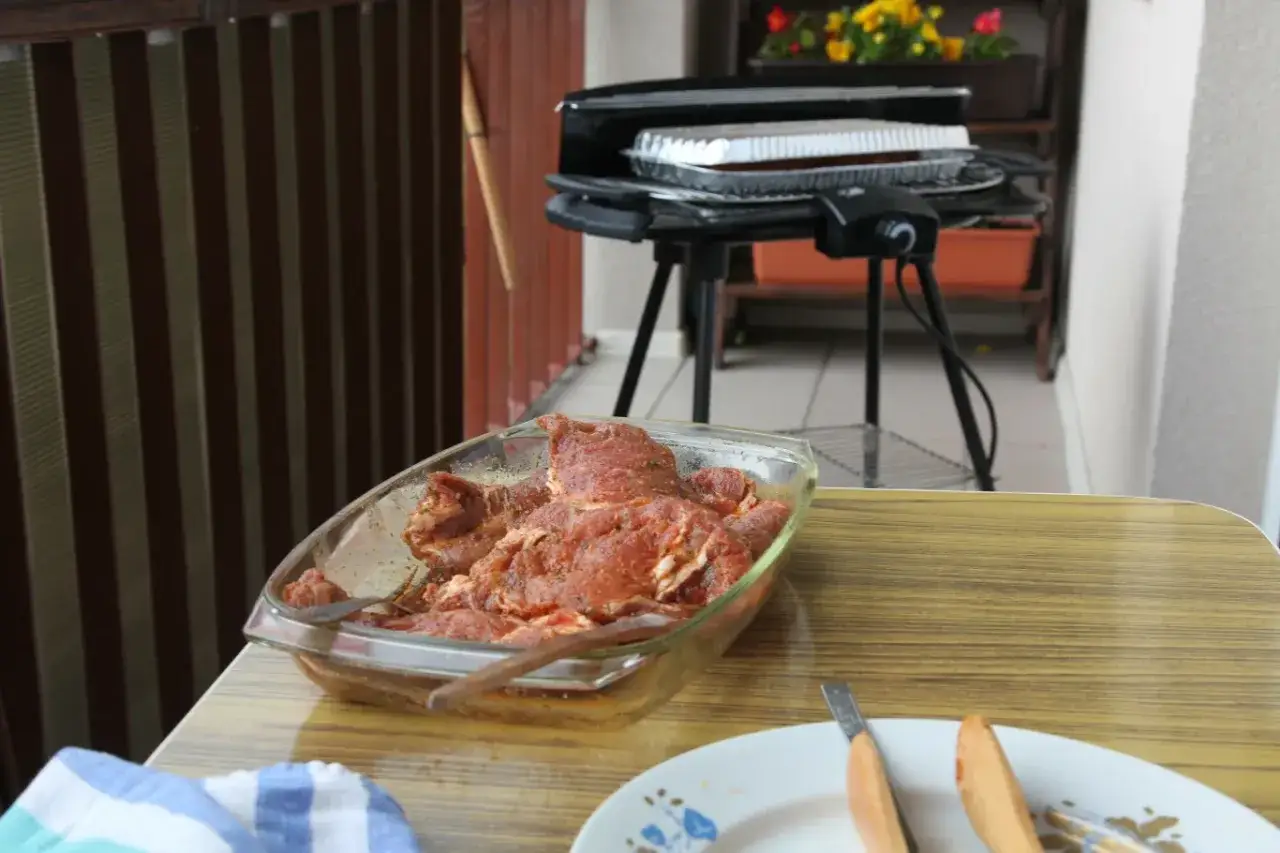 Marynowane mięso czeka na grillu na balkonie. Czy można grillować na balkonie? Tak, jeśli masz odpowiedni sprzęt i przestrzegasz zasad bezpieczeństwa.