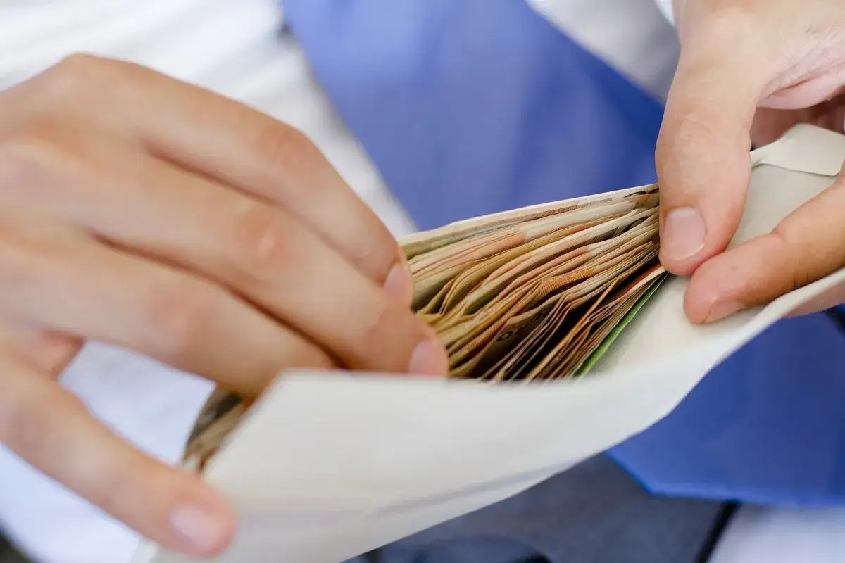 Dłonie wsuwają plik banknotów do koperty. Czy to prezent, czy może łapówka?