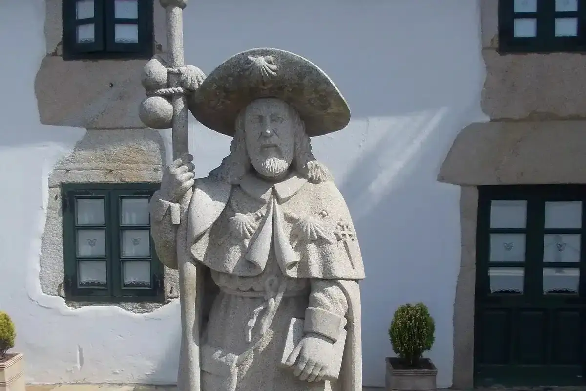 Estatua de piedra de un peregrino con sombrero de ala ancha y bord&oacute;n, s&iacute;mbolo del Camino de Santiago. Un d&iacute;a soleado de san Jaime.