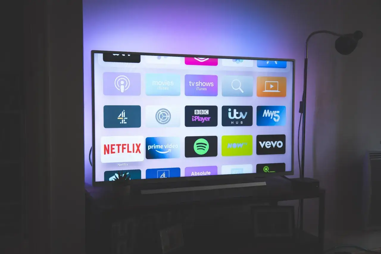 Nowoczesny telewizor z podświetleniem ambientowym, wyświetlający ekran główny z ikonami aplikacji streamingowych, takich jak Netflix, Prime Video, Spotify, BBC iPlayer. To właśnie qned co to za technologia, która zapewnia tak żywe kolory.