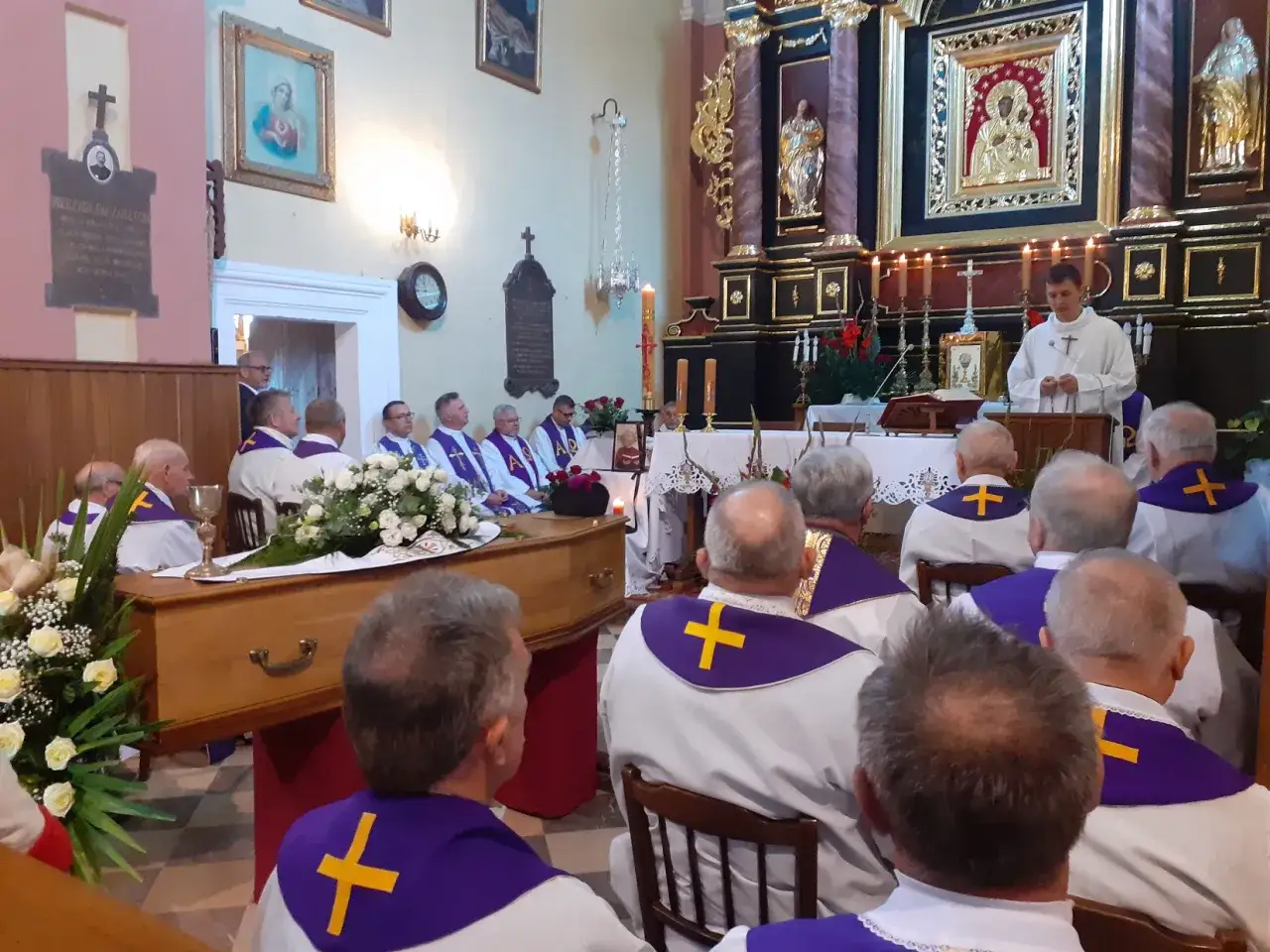 Uroczystość pogrzebowa w kościele. Ksiądz odprawia mszę przy trumnie, otoczony przez duchownych. Wiele osób zastanawia się, ile bierze kościelny za pogrzeb.