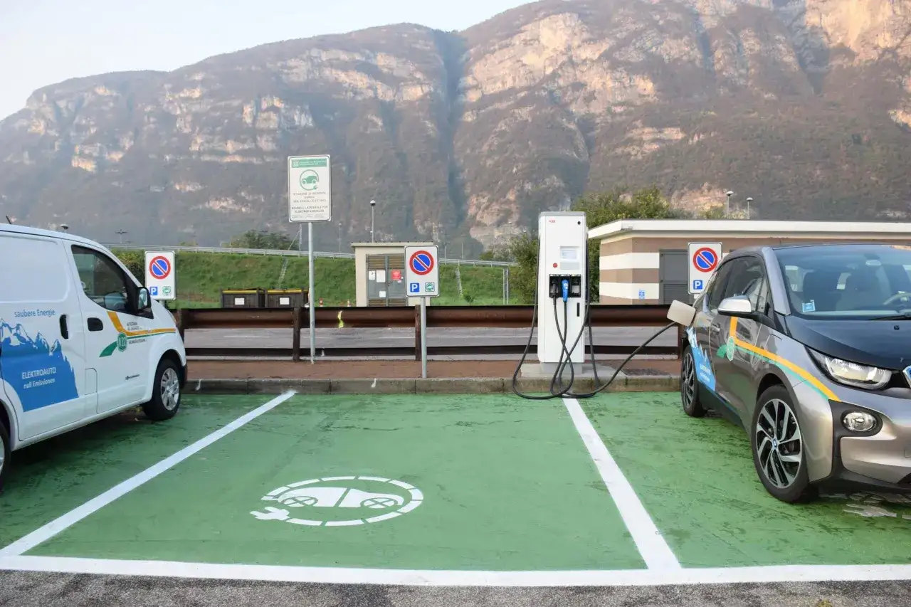 Stazione di ricarica per auto elettriche, con colonnina e due veicoli in carica. La normativa parcheggi auto elettriche è ben visibile.