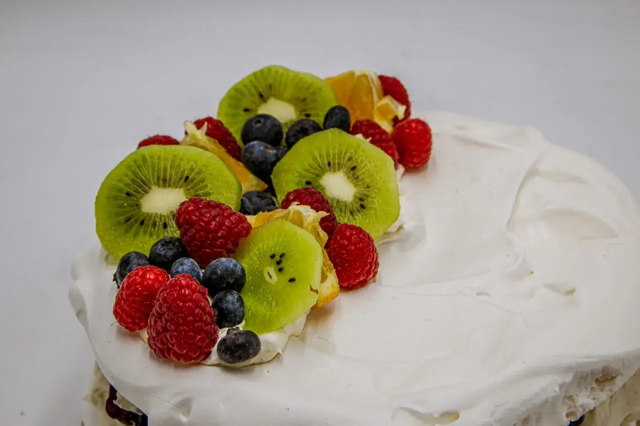 Pyszny tort bezowy z owocami: kiwi, malinami i borówkami. Zastanawiasz się, ile kosztuje tort bezowy w cukierni?