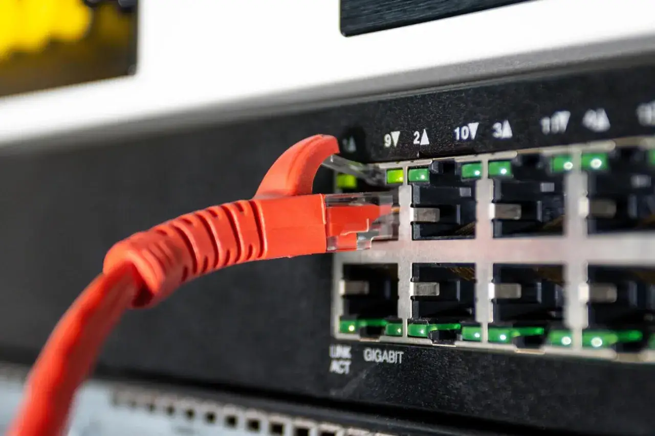 Czerwony kabel sieciowy podłączony do portu ethernet na przełączniku sieciowym. Zielone diody sygnalizują aktywność.