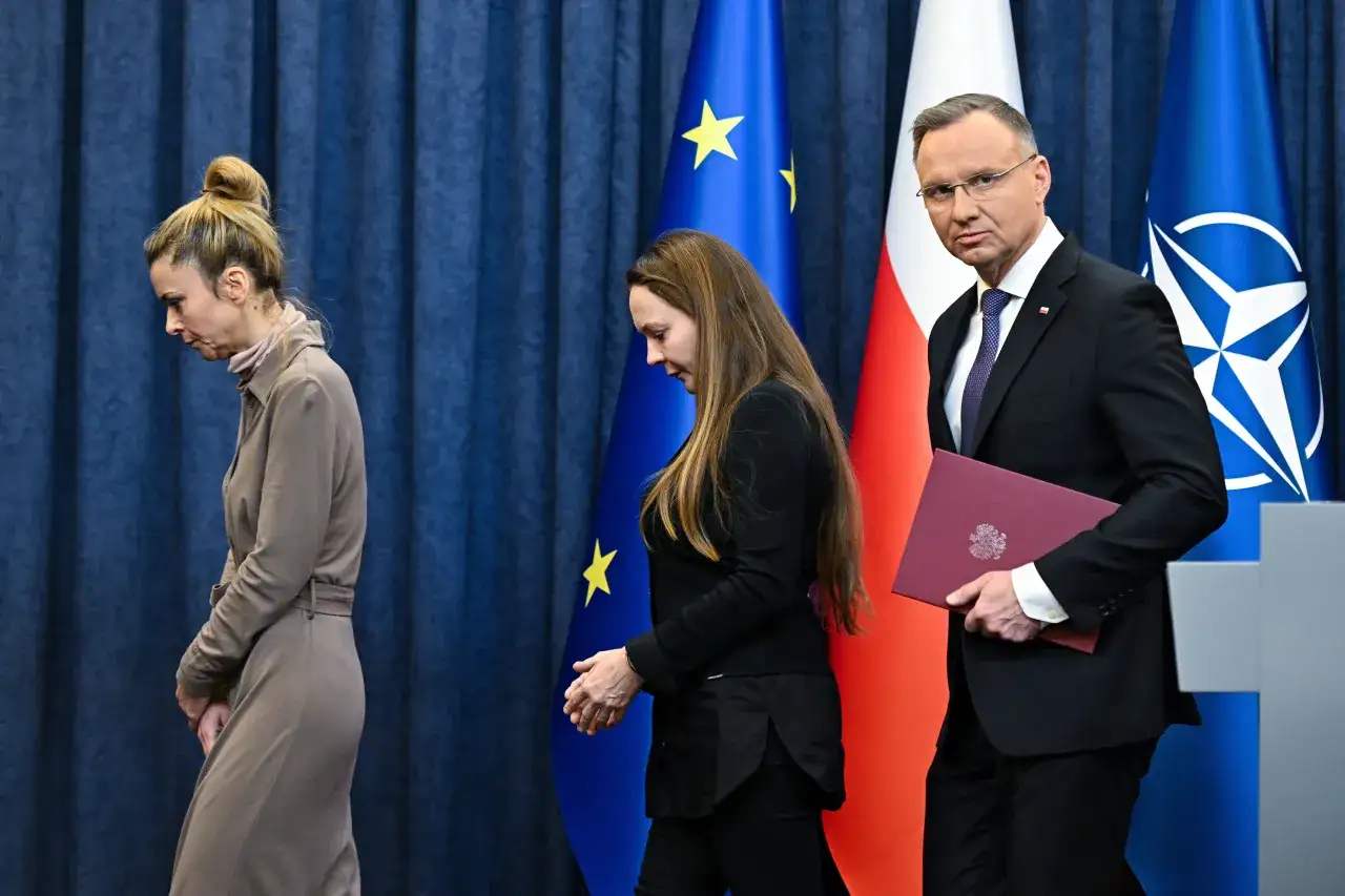 Prezydent Duda z dokumentem, obok flagi Polski, UE i NATO. Dwie kobiety w tle. Czy to odpowiedź na pytanie, dlaczego prezydent odmówił ułaskawienia znanych polityków mimo nacisków własnej partii?