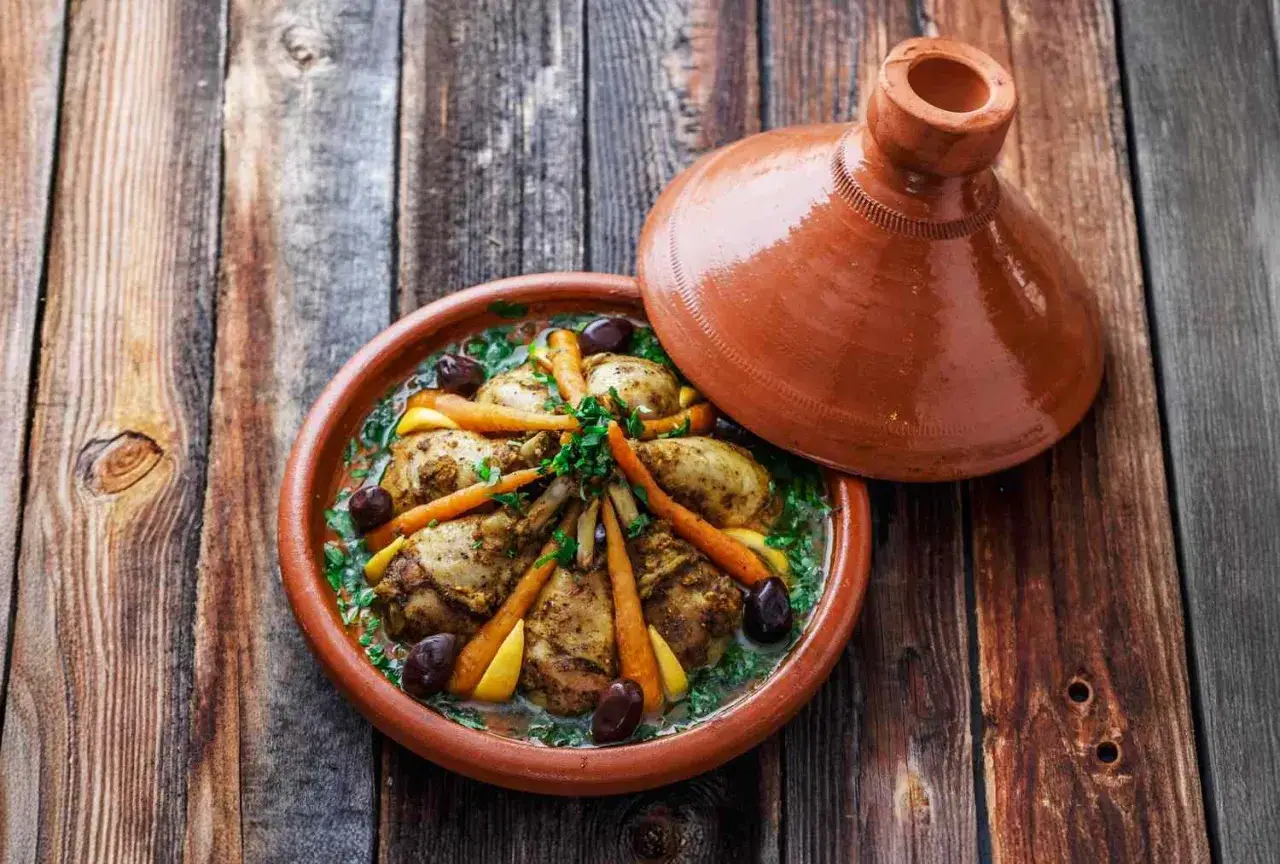Ein k&ouml;stliches H&auml;hnchen-Tajine mit Karotten, Oliven und Zitrone, serviert in einem traditionellen Tontopf.