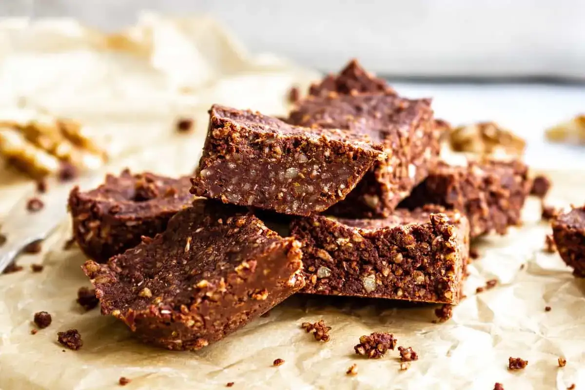 Gestapelte, rustikale Rohkost-Brownies mit Nüssen und Kakao auf Backpapier. Ein gesunder Genuss!