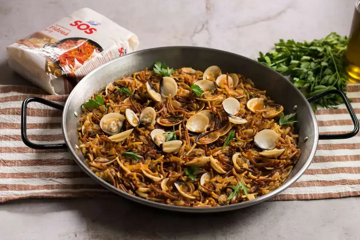 Fideu&aacute; con almejas reci&eacute;n hecha en paellera, lista para disfrutar. Un plato marinero lleno de sabor.