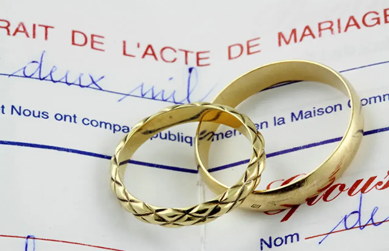 Deux alliances dor&eacute;es reposent sur un acte de mariage, symbolisant l'union et le d&eacute;but d'une nouvelle vie. Un clin d'&oelig;il &agrave; votre g&eacute;n&eacute;afrance mariage.